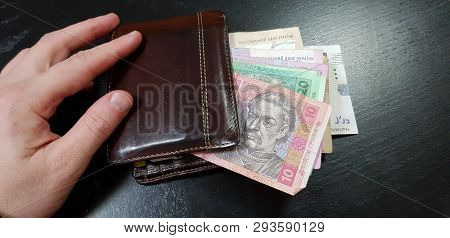 Brown Leather Wallet Full With Hryvnia Banknotes With Male Fingers On It Lay On Black Table