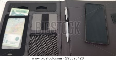 Black Smart Phone Lay On Open Leather Folder With A Pen And Serbian Paper Money In Pockets