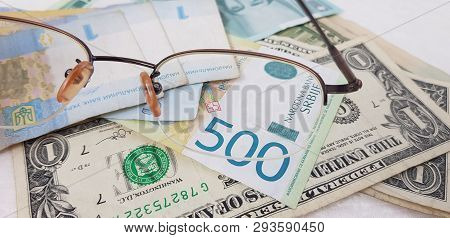 Banknotes Of Hryvnia Dynars And Dollars Seen Through Eyeglasses On White Table