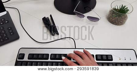 Female Hand On Black Computer Keyboard Near Office Phone Stepler Glasses And Succulent Artificial Pl