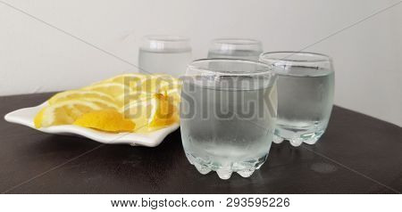 Four Glasses With Vodka On Brown Table Around White Plate With Lemon Slices