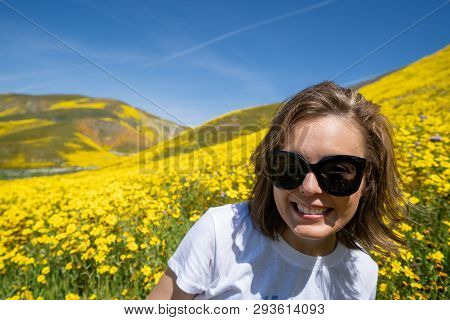 Woman Wearing Sunglasses Sits And Poses In A Field Of Yellow Wildflowers At Carrizo Plain National M