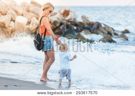 Woman Playing With Her Baby Outside Against The Sea. The Concept Of A Happy Full-fledged Family Life
