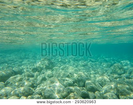 Underwater View Of Turquoise Clear Water And White Pebbles Scattered Off The Seabed Of The Antisamos