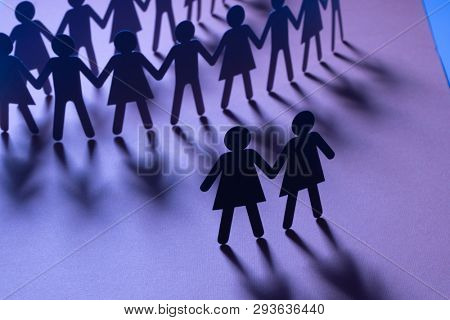 Black paper figure of a female couple in front of a crowd of paper people holding hands on blue surface. Social movement, minorities, same-sex marriage concept.