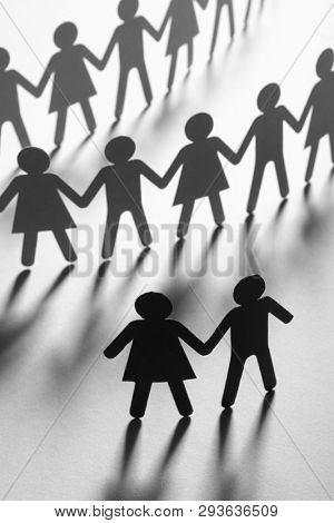 Black paper figure of a couple in front of a crowd of paper people holding hands on white surface. Social movement, protest, leadership concept.