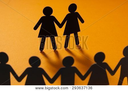 Black paper figure of a female couple in front of a crowd of paper people holding hands on orange background. Social movement, minorities, same-sex marriage concept.