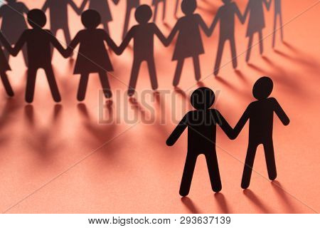 Black paper figure of male couple in front of a crowd of paper people holding hands on redsurface. Social movement, protest, minorities concept.