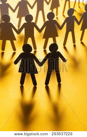 Black paper figure of a couple in front of a crowd of paper people holding hands on yellow surface. Social movement, protest, leadership concept.