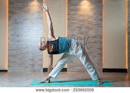 Sports man looking up with raised arm doing yoga on blue mat.