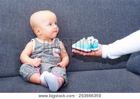 A Girl About One Year Old Is Sitting On The Couch; She Is Stretched By A Hand With Booties For A Boy