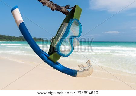Blue Mask And Snorkel Hangs On A Tree Branch Against The Backdrop Of The Sea And The Beach. Vacation