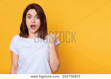 Close Up Portrait Of Beautiful Brunette Girl Shows Something Aside With Thumb, Astonished Woman Poin