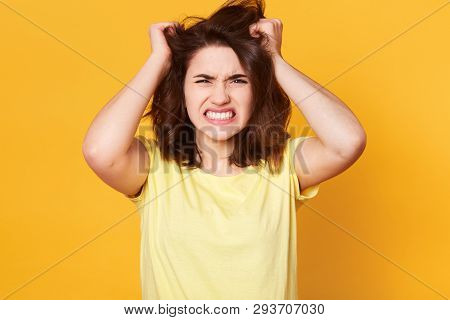 Attractive Brunette Female Scrathes Head And Exclaims Loudly, Looks Angry, Wears Casual T Shirt, Pos