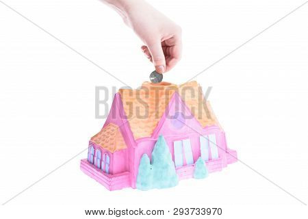 Hand Drops A Coin Into The Piggy Bank House On A White Background, Shallow Depth Of Field