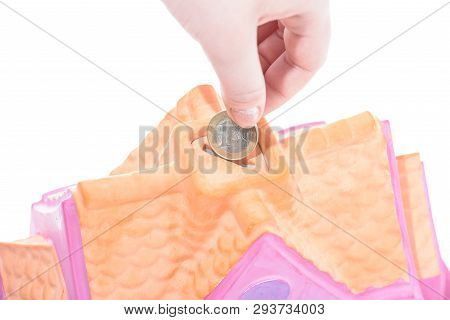 Hand Drops A Coin Into The Piggy Bank House On A White Background, Shallow Depth Of Field