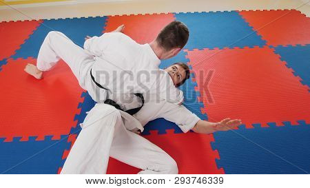 Two Men Training Their Aikido Skills In The Studio. A Man Grabs His Opponent And Throws Him On The F