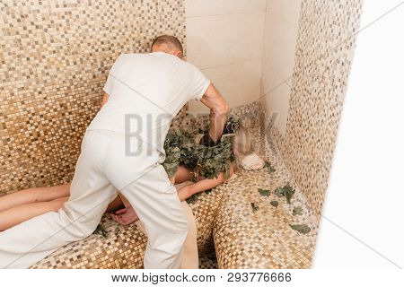 Slim Woman In Bath Is Getting Steaming Massage With Hot Oak Leaves Brooms, In Steam-room