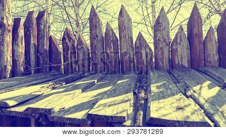 Fence Made Of Sharp Wooden Stakes Against The Sky. Ancient Stockade. Toned.