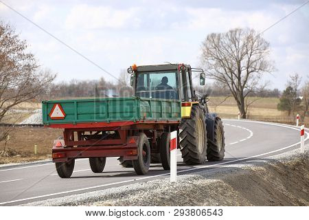 A Tractor With A Trailer Rides On An Asphalt Road. Rear View Of Agricultural Transport. Transportati