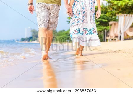 The Man And The Women Hold One Hand On The  Beach And Front Of Sunset.thay Are Couple. They Are Walk
