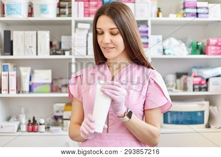 Dermatologist Doctor Holds Cream In White Tube. Attractive Cosmetologist Prepares For Cosmetic Proce
