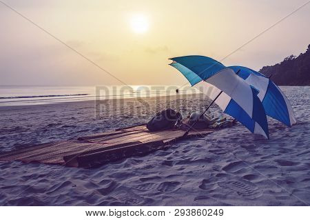 Two Umbrellas Of White And Blue Color Lying On A Deserted Deserted Beach On The Background Of A Beau