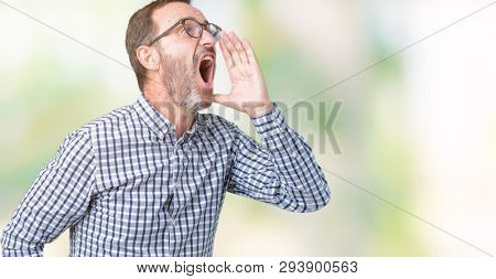 Handsome middle age elegant senior business man wearing glasses over isolated background shouting and screaming loud to side with hand on mouth. Communication concept.