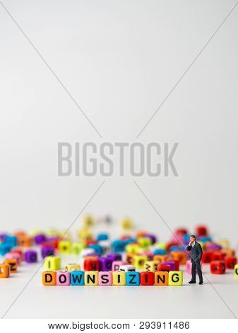 Miniature Figure Businessman In Dark Blue Suit Standing Backside Of Colorful Of Downsizing Alphabet 