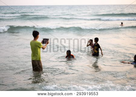 Ko Chang, Thailand - April 10, 2018: Thay Asian Children Playing In Sea - Boy Takes Photo Via A Tabl