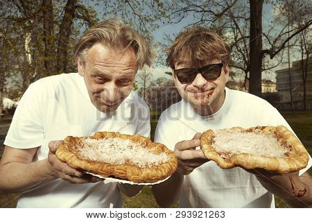 Men In Street Park Eating Langos With Garlic, Ketchup And Cheese