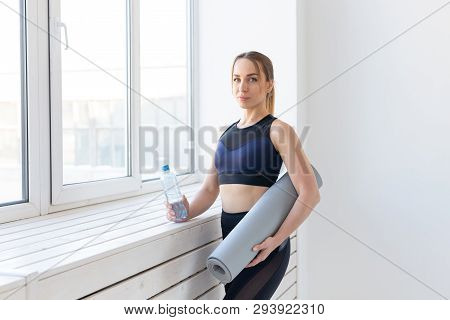 People, Sport And Fitness Concept - Young Woman With Yoga Mat And Bottle Of Water Standing Near Wind