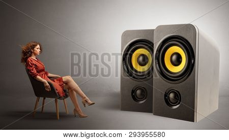 Stylish young lady sitting in a sofa and listening to big loudspeakers