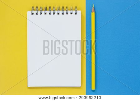 Open Blank Notepad With A Yellow Pencil, On A Blue And Yellow Flat Lay Background