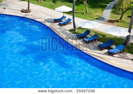 Swimming pool with chaise lounge and sunshade at tropical resort