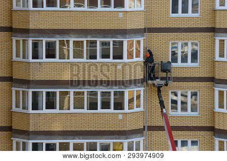 Worker On An Autotower Repairs The Facade Of An Apartment Brick Residential Building