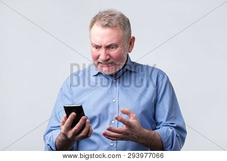 Annoyed Senior Man In Blue Shirt Looking At Mobile Phone
