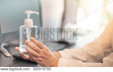 The Female Hand Holding Alcohol Bottle Gel With The Computer Laptor And Alcohol Gel Put On Beside Th