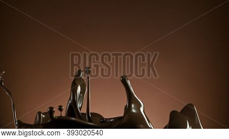 Splash of molten chocolate on gradient brown background, cllose-up.