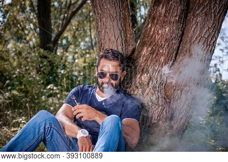 Bearded Smoker Enjoying An Electronic Cigarette In The Calm Outdoors. Hybrid Cigarette.