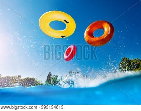 Action Photo In The Outdoor Swimming Pool With Splashes And Waves Of Inflatable Doughnuts Buoys Ring