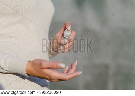 Girl Disinfects Her Hands With Antiseptic. Against The Background Of A Gray Concrete Wall.