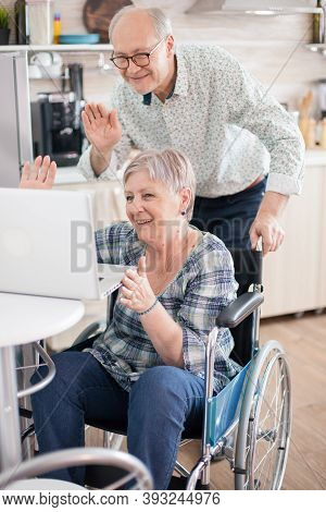Senior Couple Laughing And Waving During A Video Call With Grandchildrens Using Tablet Computer In K