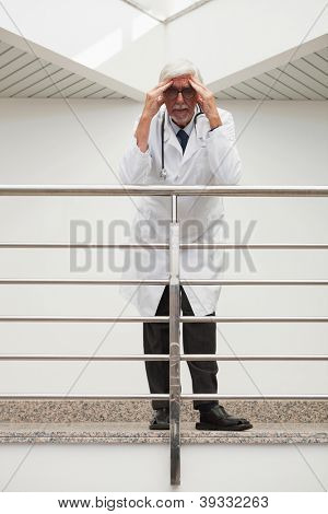 Stresli doktor hastane koridorda ise onun alnında el ile korkuluk üzerine eğilerek