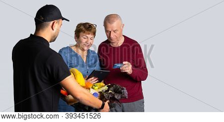 Banner, Long Format. An Elderly Family Pays For Courier Delivery By Credit Card. Photo Over White Ba