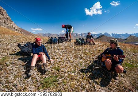 Group Of Trekkers Resting And Playing Guitar In Rocky Pass With Mountain Top Wiews In High Mountains
