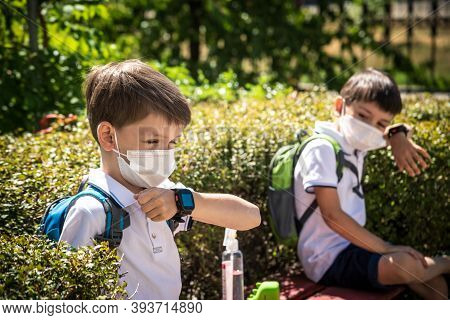 Coronavirus School Reopening Concept: A School Boys Sit On Bench In Front Of A School Wearing A Face