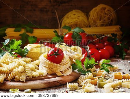 Assorted Dry Pasta, Cherry Tomatoes And Parsley On A Vintage Wooden Background, Selective Focus