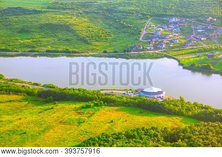 Village Situated On The Lakeside . Aerial View Of Spring Green Meadow And Lake