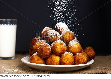 Fried Donuts Are Sprinkled With Powdered Sugar. There Is A Glass Of Milk In The Background